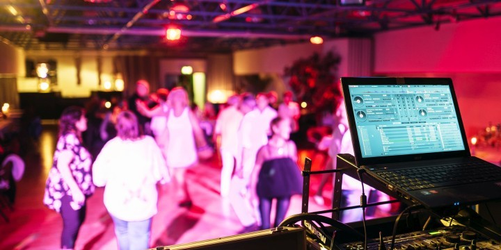 Tanzende Menschen in einem Veranstaltungsaal, im Vordergrund ein DJ-Laptop
