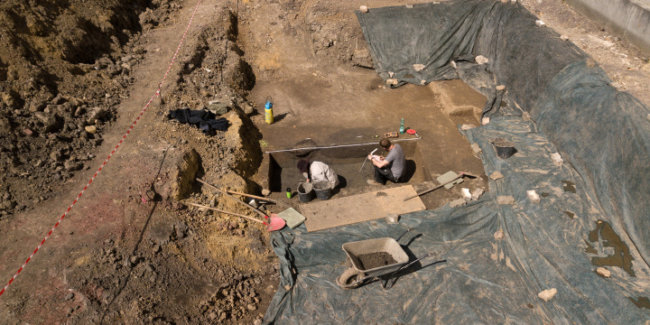 Eine Ausgrabungsaustelle, in der zwei Archöologen sitzen, graben und etwas notieren.  ©Uwe Germar